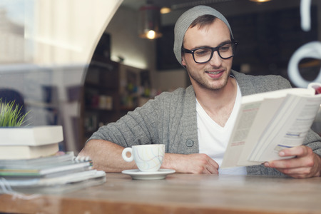 28284680 – smiling hipster man reading book at cafe